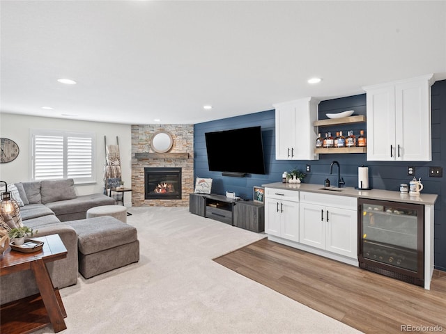 living room featuring beverage cooler, bar with sink, a stone fireplace, light wood finished floors, and recessed lighting