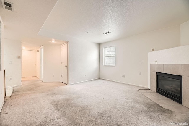 unfurnished living room featuring a tile fireplace, light carpet, and a textured ceiling