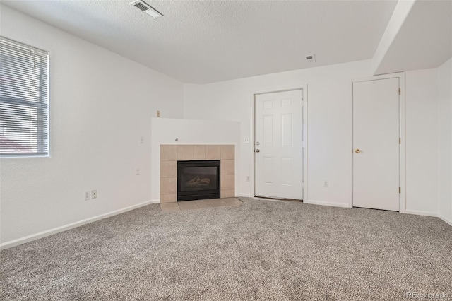 unfurnished living room featuring light carpet, baseboards, visible vents, a tile fireplace, and a textured ceiling