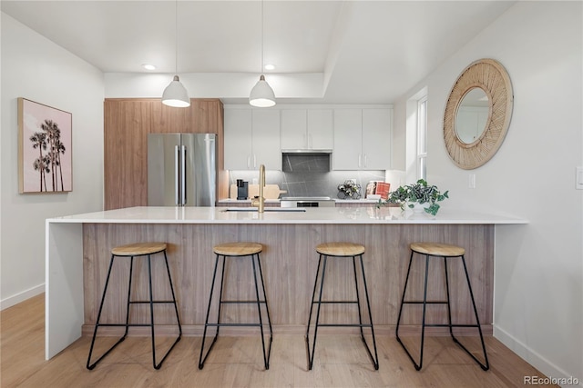 kitchen with stainless steel fridge, white cabinets, sink, and a kitchen bar