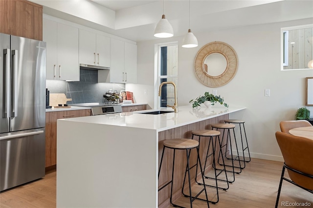 kitchen featuring a breakfast bar, a peninsula, freestanding refrigerator, a sink, and light wood-type flooring