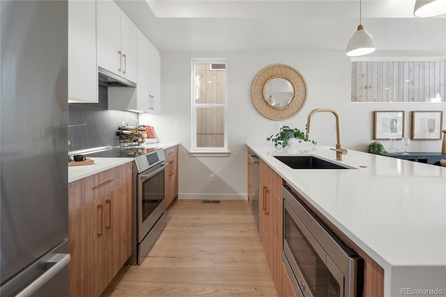 kitchen with light wood-type flooring, a sink, tasteful backsplash, appliances with stainless steel finishes, and light countertops