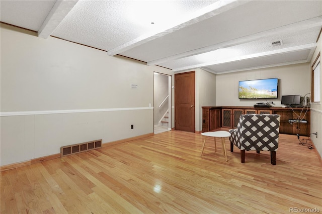 unfurnished room with beam ceiling, light hardwood / wood-style floors, and a textured ceiling