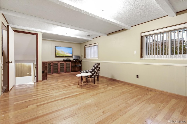 living area featuring beam ceiling, light wood-type flooring, and a textured ceiling