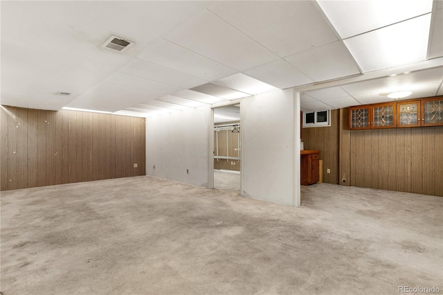 basement with a drop ceiling, wooden walls, and carpet