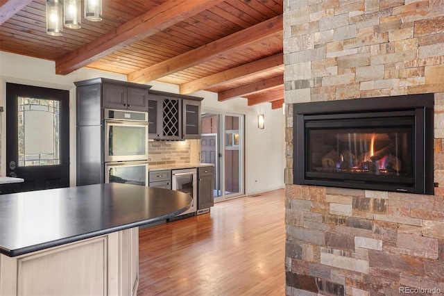 kitchen featuring a stone fireplace, wine cooler, hardwood / wood-style flooring, double oven, and beamed ceiling