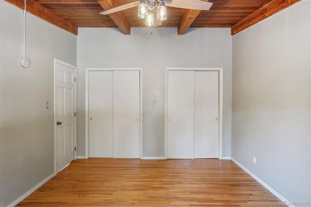 unfurnished bedroom with beam ceiling, multiple closets, ceiling fan, and wooden ceiling