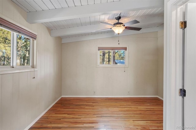 empty room featuring lofted ceiling with beams, a wealth of natural light, ceiling fan, and light hardwood / wood-style floors