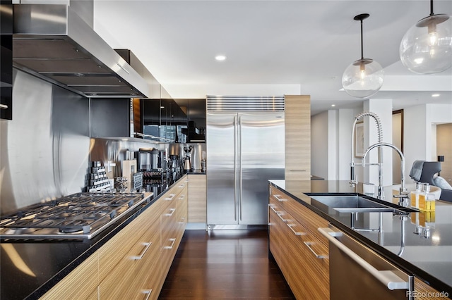 kitchen with dark hardwood / wood-style floors, sink, hanging light fixtures, wall chimney exhaust hood, and stainless steel appliances