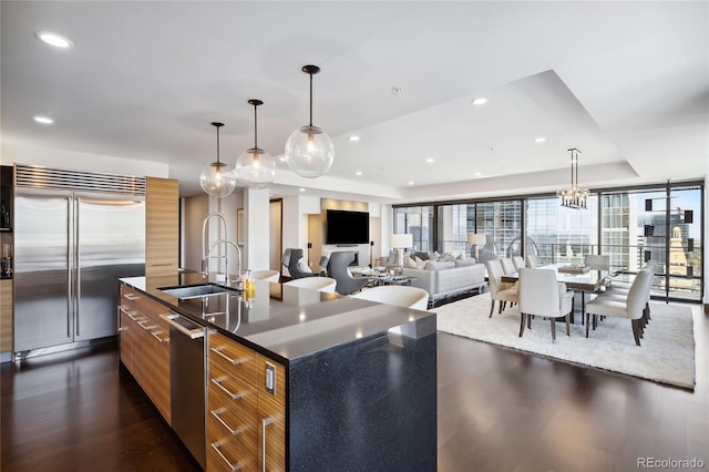 kitchen featuring dark hardwood / wood-style flooring, stainless steel appliances, decorative light fixtures, a center island with sink, and sink