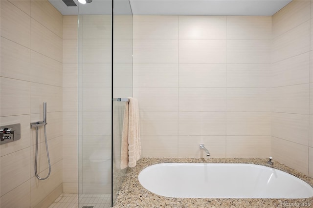 bathroom featuring independent shower and bath and tile walls