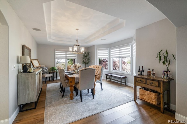 dining room with wood finished floors, a raised ceiling, a chandelier, arched walkways, and baseboards