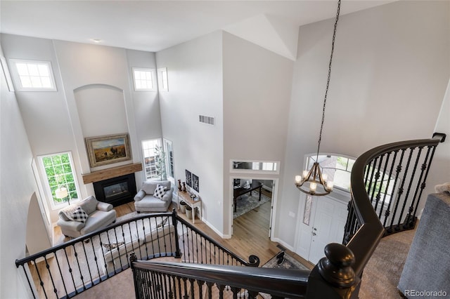 stairs with a glass covered fireplace, a high ceiling, a chandelier, wood finished floors, and plenty of natural light