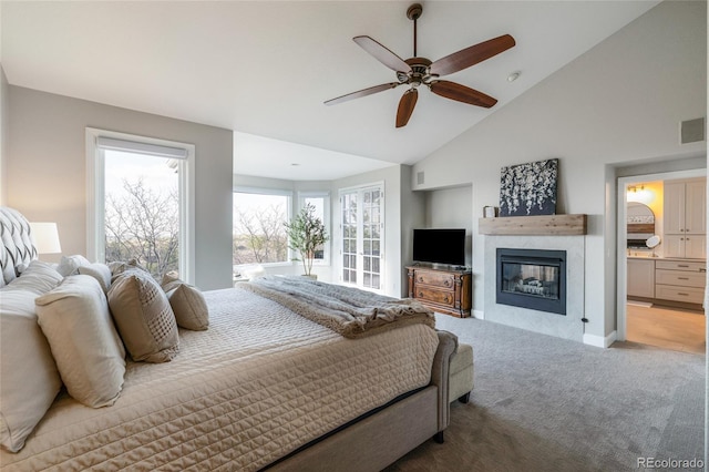 carpeted bedroom with a glass covered fireplace, ceiling fan, connected bathroom, high vaulted ceiling, and baseboards