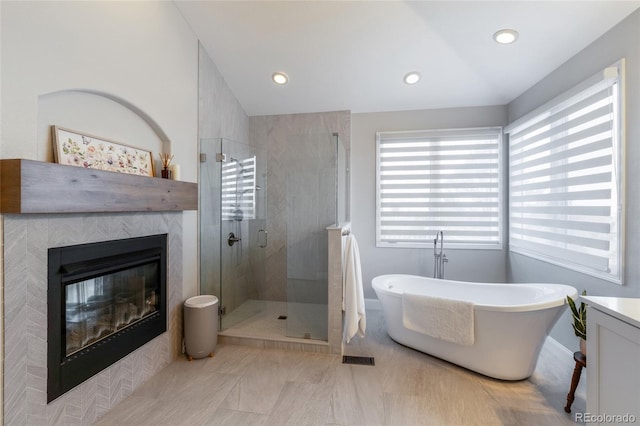 full bathroom featuring a stall shower, a freestanding bath, a glass covered fireplace, recessed lighting, and baseboards