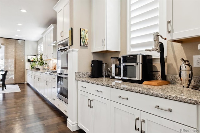 kitchen with double oven, white cabinetry, dark wood-type flooring, and light stone countertops