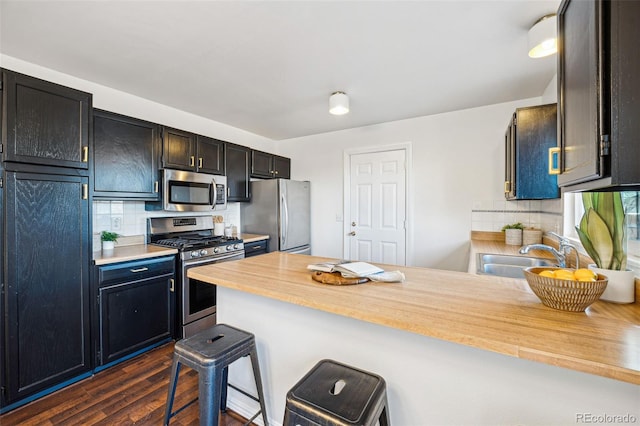 kitchen with kitchen peninsula, tasteful backsplash, appliances with stainless steel finishes, a kitchen breakfast bar, and sink