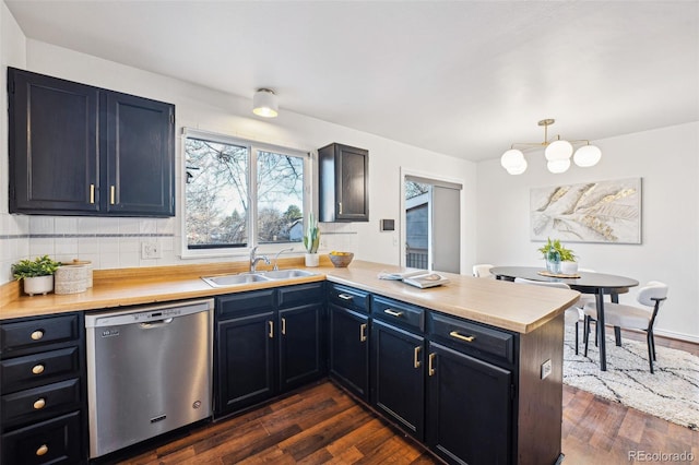 kitchen with kitchen peninsula, stainless steel dishwasher, hanging light fixtures, decorative backsplash, and sink