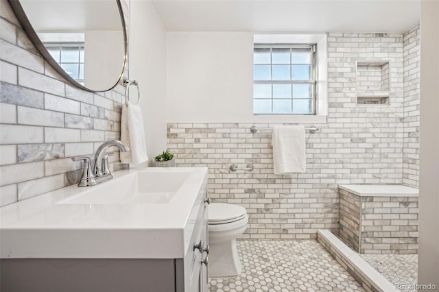 bathroom featuring toilet, vanity, a healthy amount of sunlight, and tiled shower