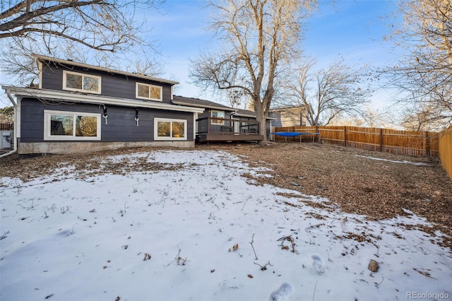 snow covered back of property featuring a wooden deck and a trampoline