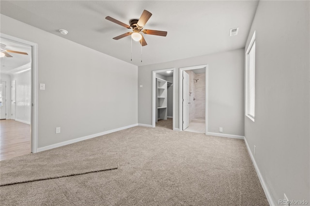 unfurnished bedroom featuring ceiling fan, a walk in closet, connected bathroom, and multiple windows