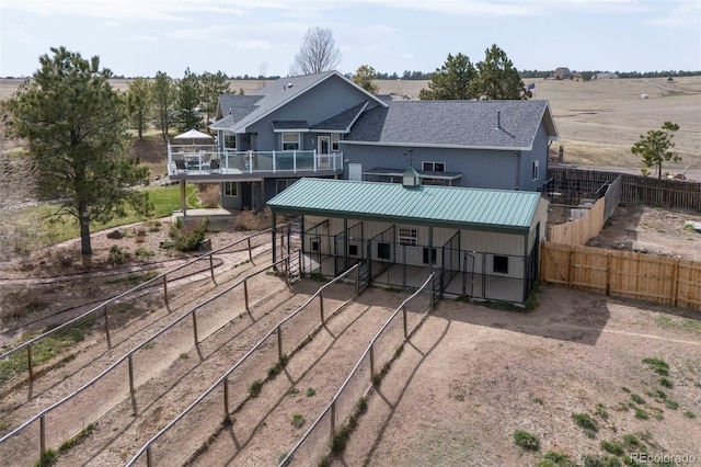 back of house featuring an outdoor structure, a shingled roof, an exterior structure, and a rural view