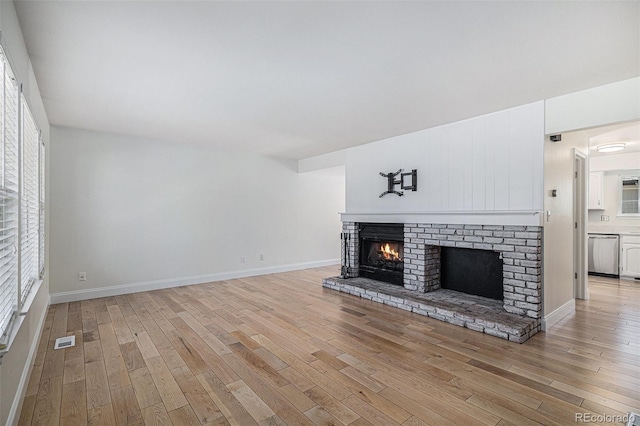 living room with light wood finished floors, plenty of natural light, a fireplace, and visible vents