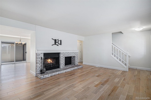 unfurnished living room with a brick fireplace, stairway, baseboards, and wood finished floors