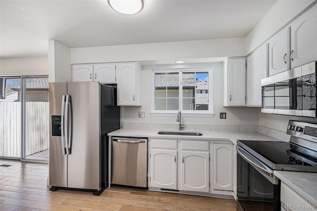 kitchen featuring light wood finished floors, stainless steel appliances, light countertops, white cabinetry, and a sink