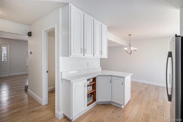 kitchen with light countertops, light wood finished floors, freestanding refrigerator, and white cabinets