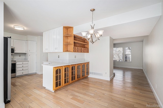 kitchen with open shelves, light countertops, light wood-style flooring, white cabinetry, and a chandelier