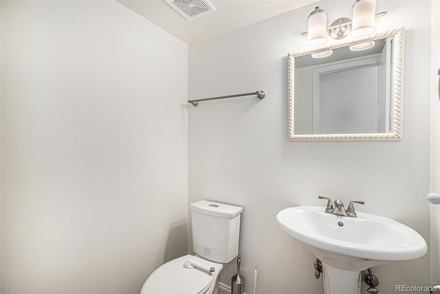 half bathroom featuring toilet, visible vents, and a sink