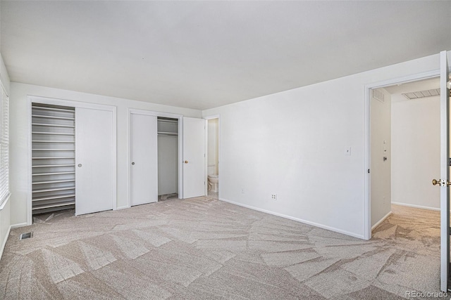 unfurnished bedroom featuring carpet, two closets, visible vents, ensuite bath, and baseboards