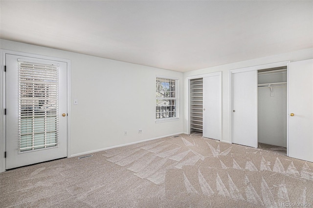 unfurnished bedroom with carpet floors, visible vents, and two closets