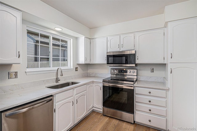 kitchen with white cabinets, light countertops, appliances with stainless steel finishes, a sink, and light wood-type flooring