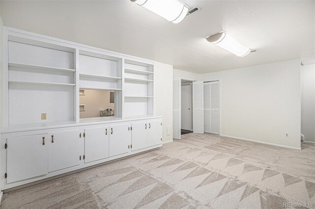 spare room featuring baseboards, light colored carpet, and visible vents