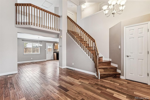 foyer with baseboards, a towering ceiling, stairway, wood finished floors, and a notable chandelier