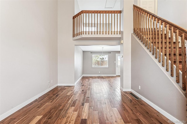 unfurnished living room with wood finished floors, a towering ceiling, visible vents, baseboards, and stairway