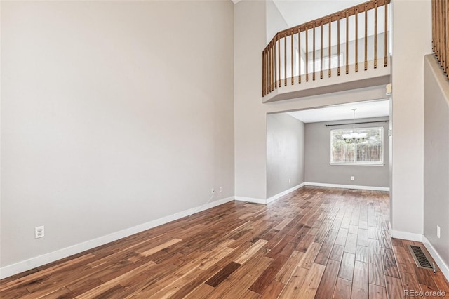 empty room featuring a chandelier, a high ceiling, wood finished floors, visible vents, and baseboards