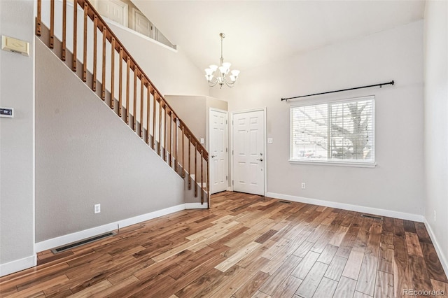 entryway with a notable chandelier, wood finished floors, visible vents, baseboards, and stairway