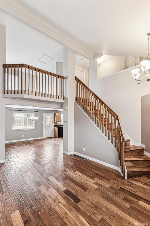 unfurnished living room with a chandelier, stairway, wood finished floors, and baseboards