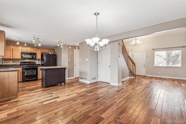 kitchen with open floor plan, black appliances, light wood finished floors, an inviting chandelier, and tasteful backsplash