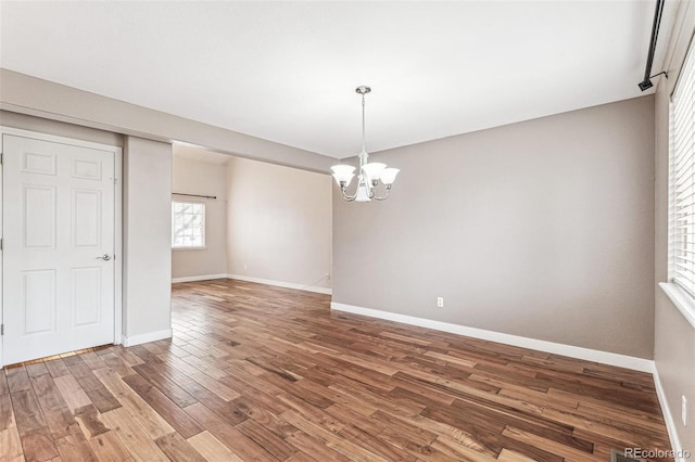 unfurnished dining area featuring baseboards, an inviting chandelier, and wood finished floors