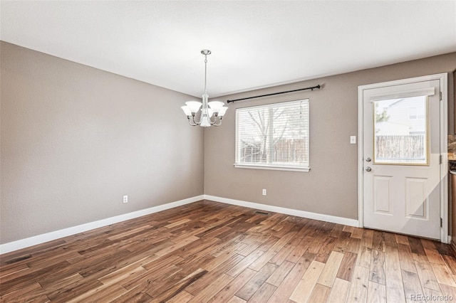 unfurnished dining area with a notable chandelier, plenty of natural light, baseboards, and wood finished floors