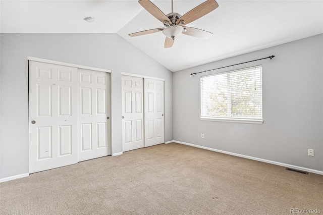 unfurnished bedroom with carpet flooring, visible vents, baseboards, vaulted ceiling, and multiple closets