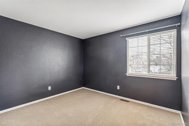 spare room featuring a textured wall, carpet flooring, visible vents, and baseboards