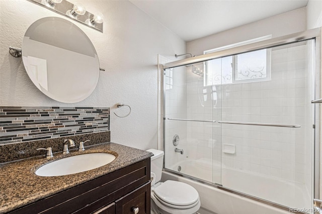 bathroom featuring decorative backsplash, a textured wall, toilet, enclosed tub / shower combo, and vanity