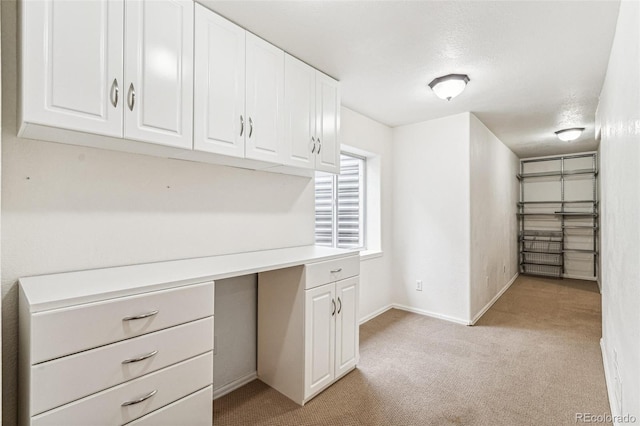 unfurnished office featuring light colored carpet, a textured ceiling, and baseboards