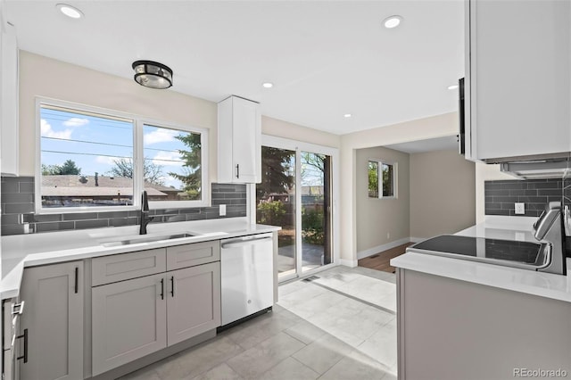 kitchen with light countertops, a sink, dishwasher, decorative backsplash, and gray cabinetry