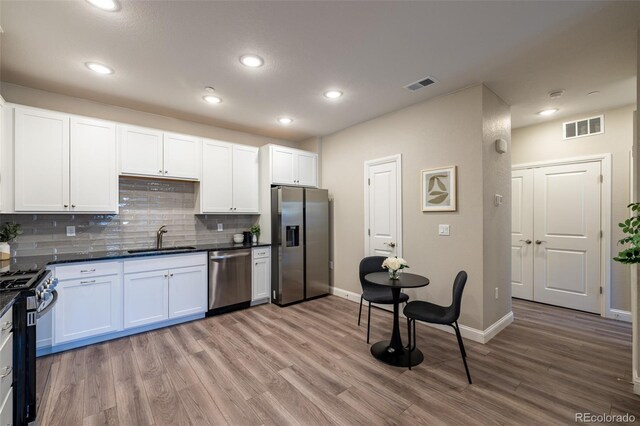 9992 W Victoria Pl Unit 103, Littleton, CO 80127 - kitchen with appliances with stainless steel finishes, dark countertops, light wood-style flooring, tasteful backsplash, and white cabinets
